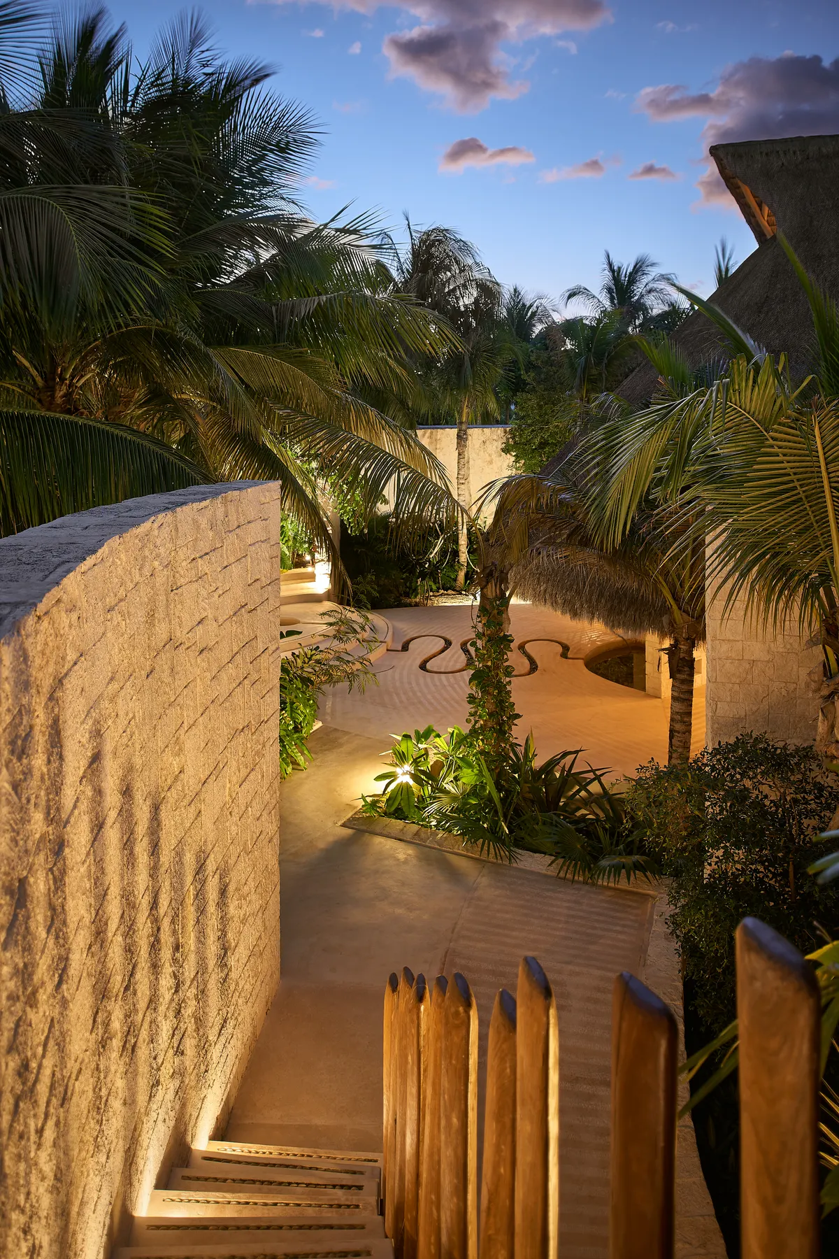 Sendero de piedra iluminado hacia la palapa al atardecer en Villa Wayak